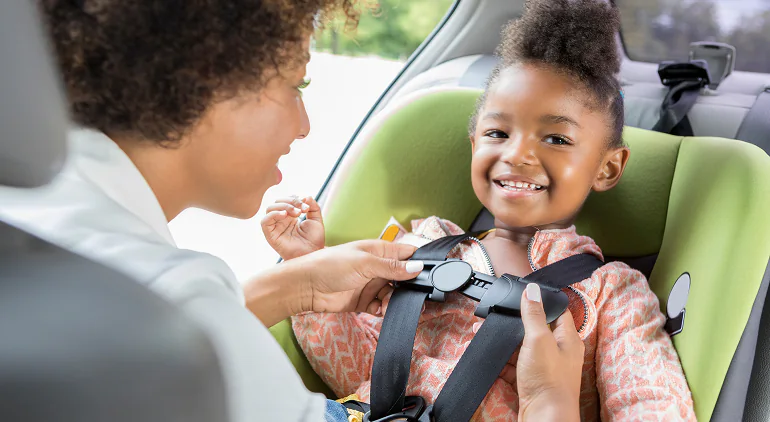 Adult buckling a smiling young child into a car seat
