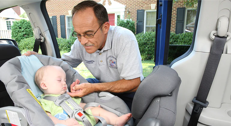 Technician installing a baby in a car seat inside a vehicle